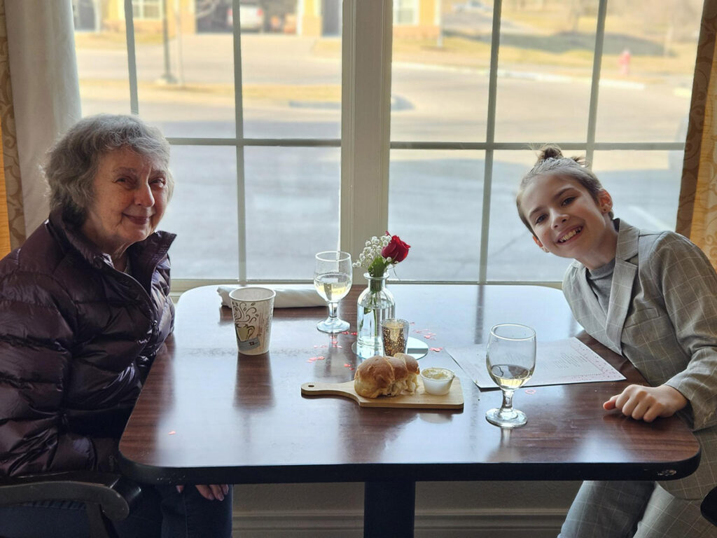 A joyful community resident and their grandchild, both beaming with excitement, eagerly anticipate a delightful lunch together.