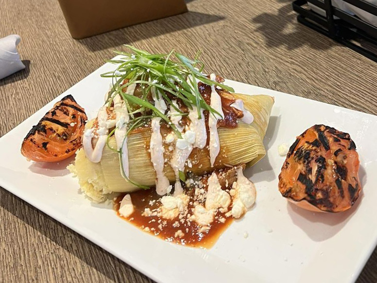 A plate with a stuffed corn tortilla topped with roja sauce, salsa verde, roasted tomato crema, cotija cheese, and fresh scallion.