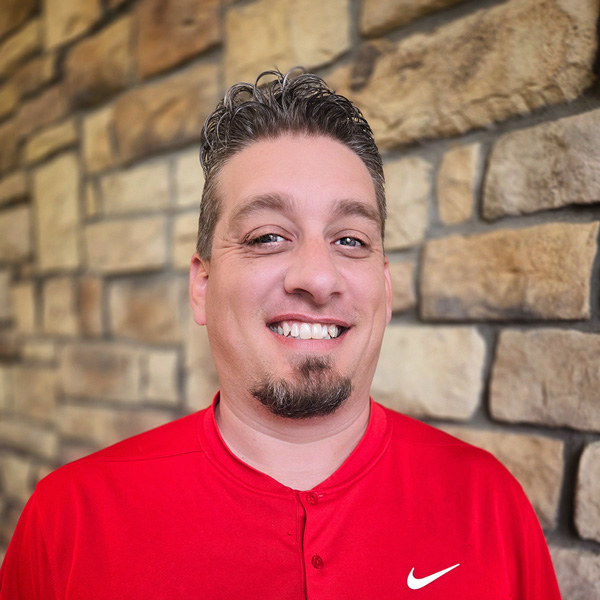 Casey Geiger, Operations Coordinator at The Parkway Senior Living, smiling in front of a stone wall, wearing a red Nike shirt.
