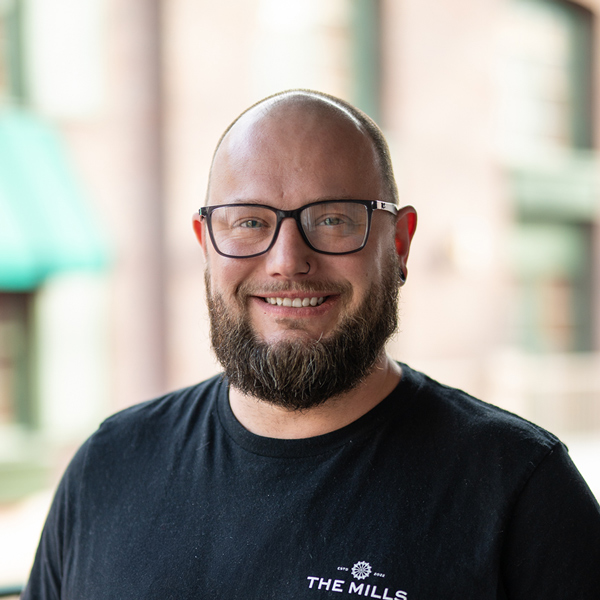 Chris Lott, Culinary Director at The Parkway Senior Living, smiling in a professional headshot, wearing glasses and a black shirt, with a softly blurred outdoor community background.
