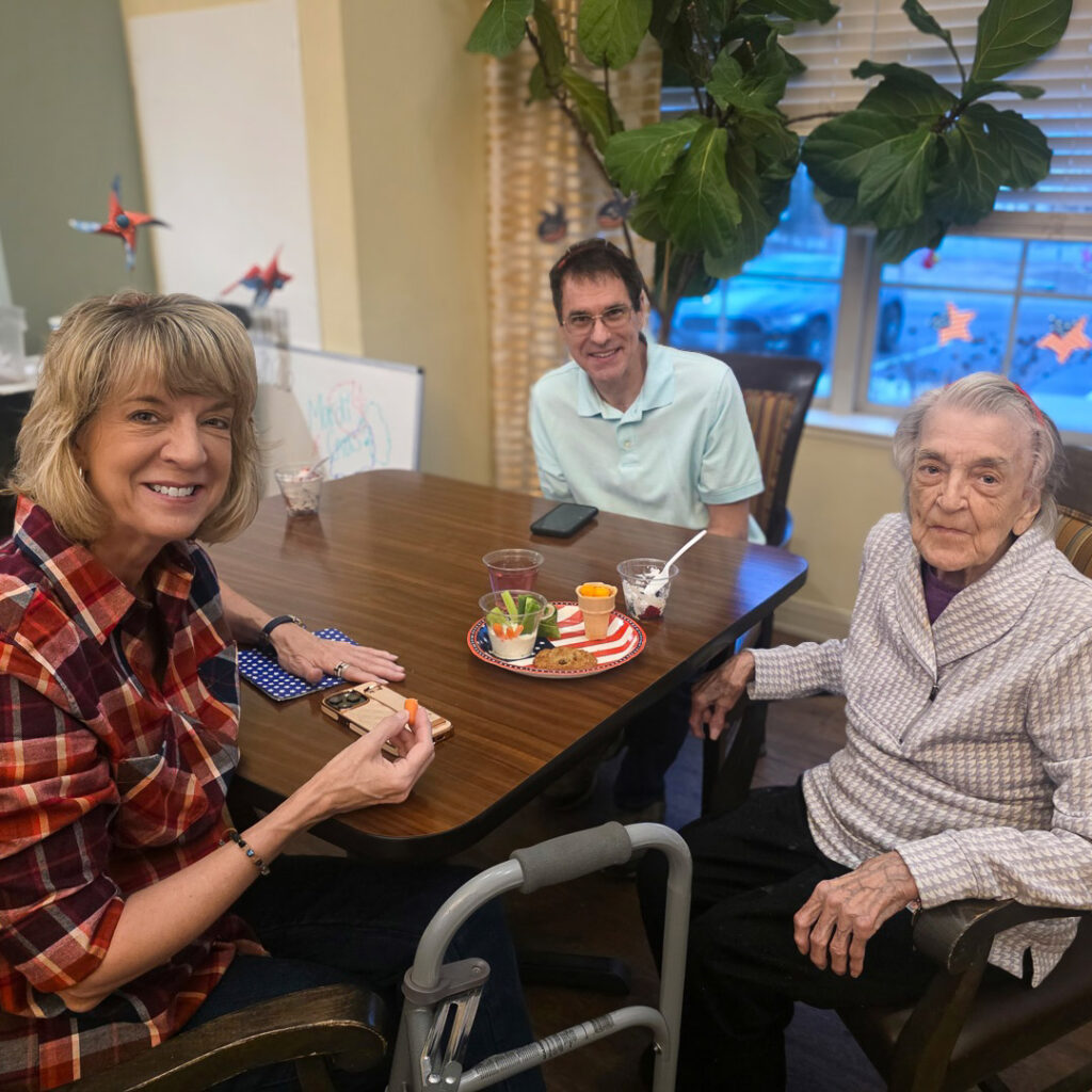 A senior resident and loved ones smile, enjoying a meal together.