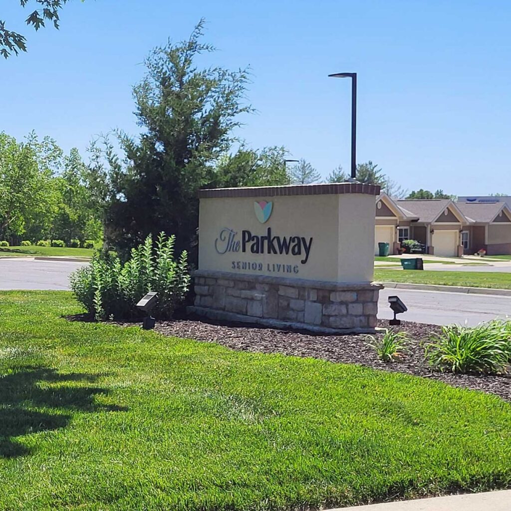 The exterior sign for The Parkway Senior Living, landscaped with many plants.